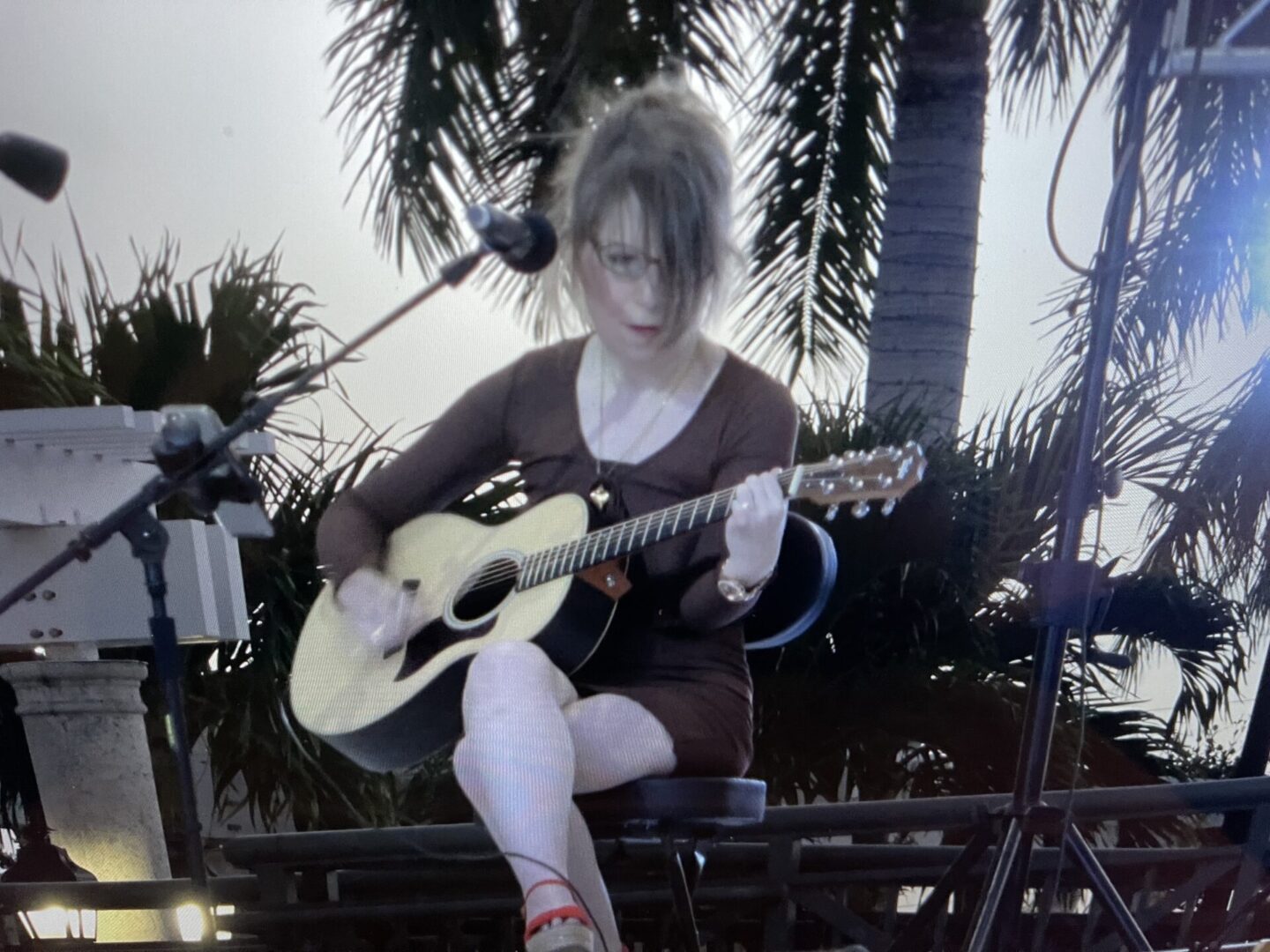 A woman sitting on top of a bench playing an acoustic guitar.