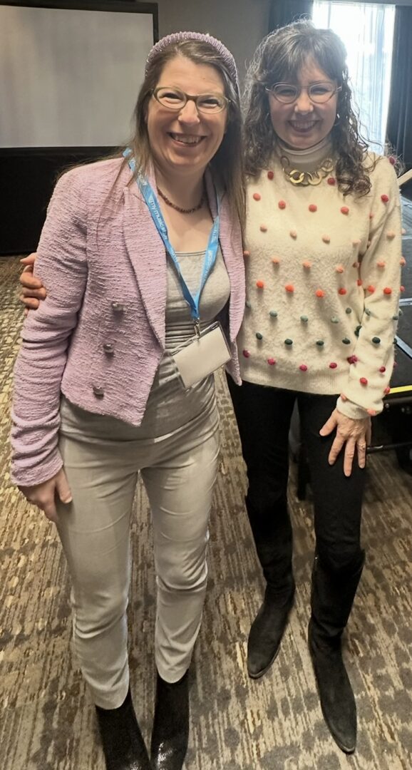 Two women smiling, standing together indoors.