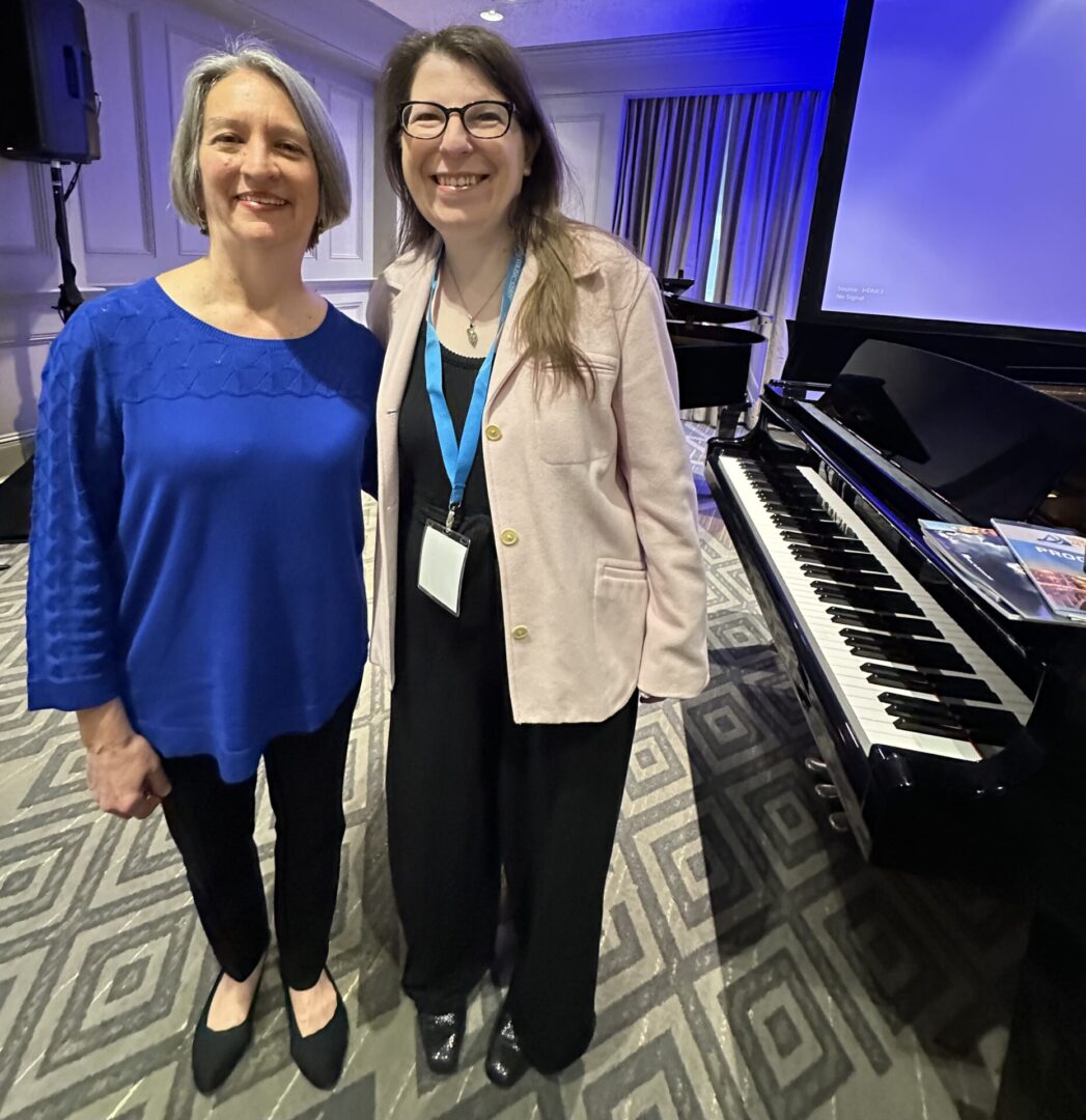 Two women smiling beside a grand piano.